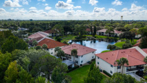 aerial view of condominium buildings around retention pond with many trees on the outside