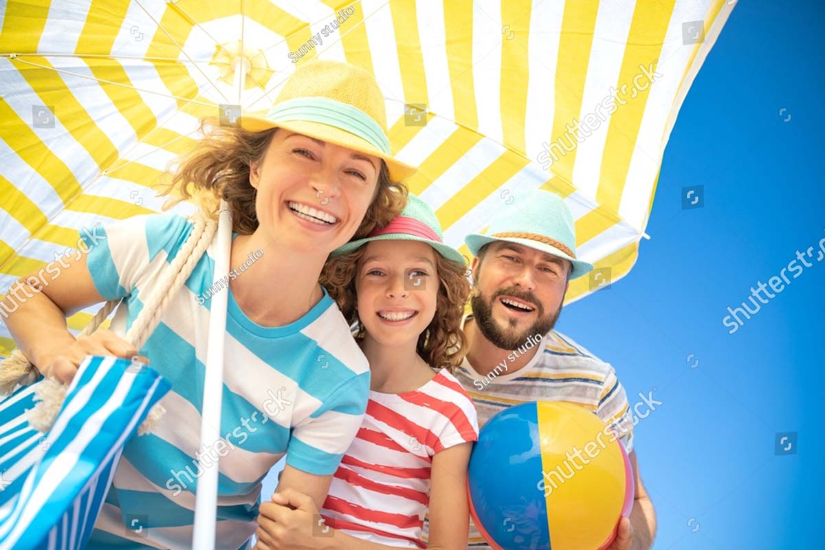 family wearing striped shirts standing under a yellow beach umbrella